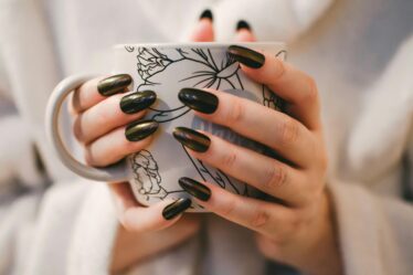 Woman with black manicure holding white and grey floral ceramic cup