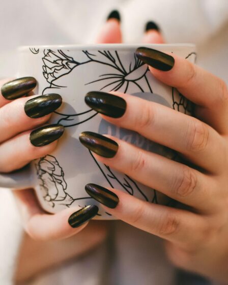 Woman with black manicure holding white and grey floral ceramic cup