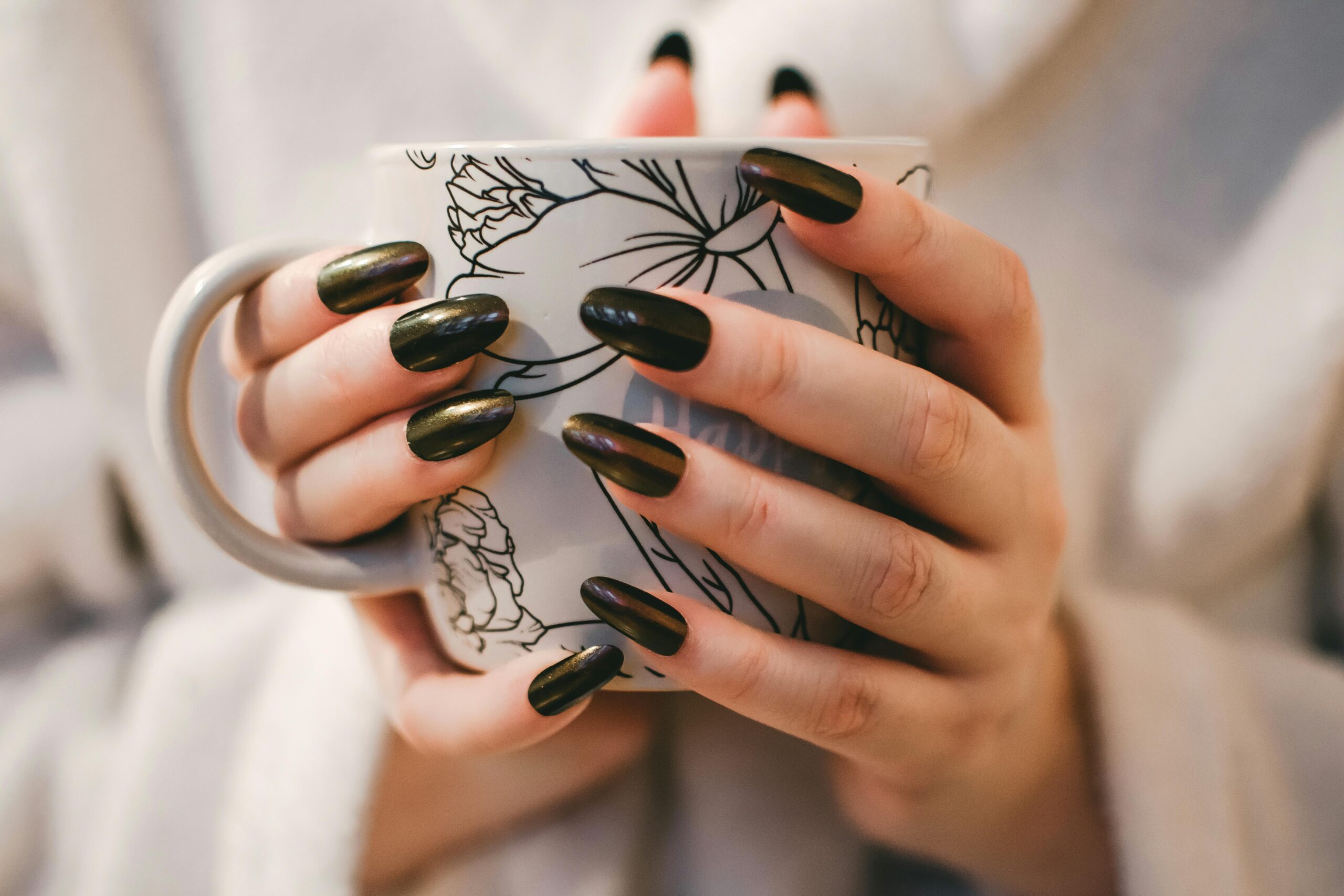 Woman with black manicure holding white and grey floral ceramic cup